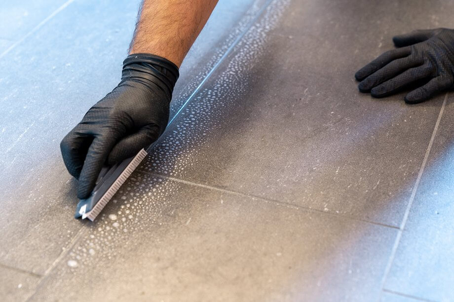 a man's hands using a tile brush to scrub grey tile