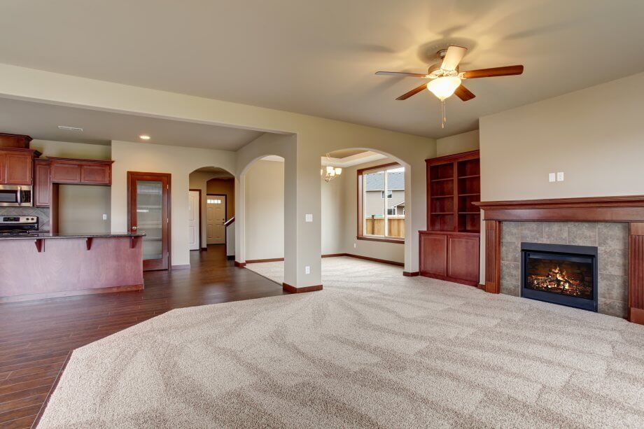 Large empty living room with freshly cleaned carpet, and fireplace.