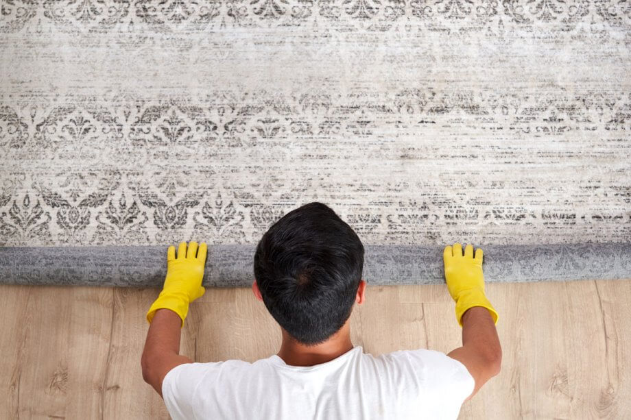 man rolling up a rug, revealing wood flooring