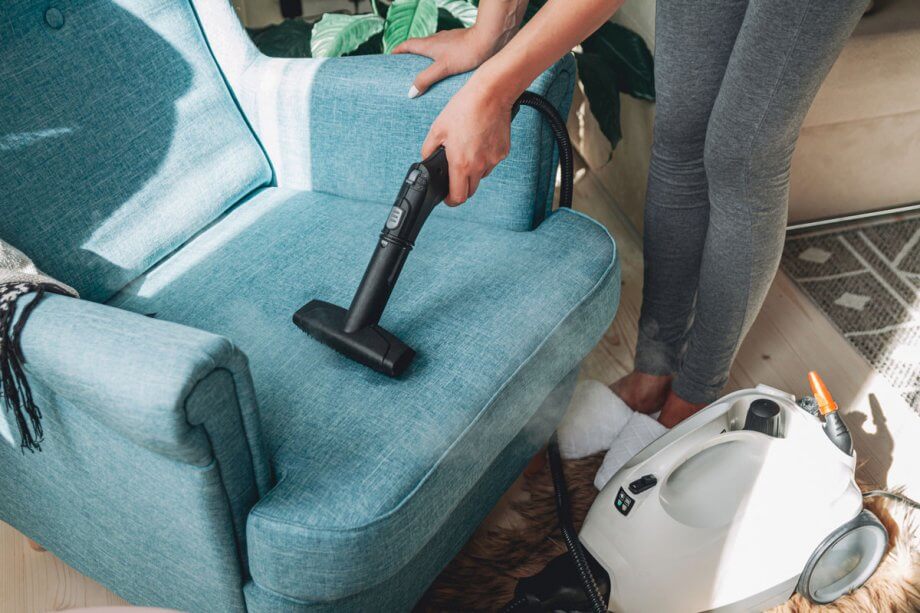 woman using a vacuum attachment to vacuum a blue chair